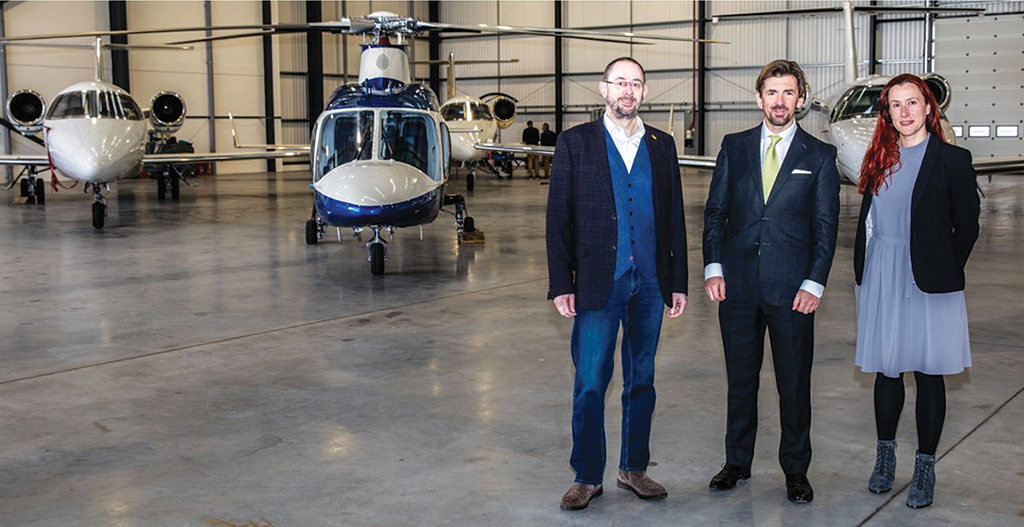 Three people stand in front of aircraft in facility