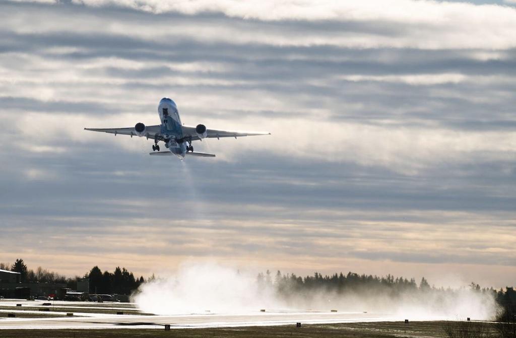 A Boeing 777 climbs away from snow on Paine Field Everett runway.